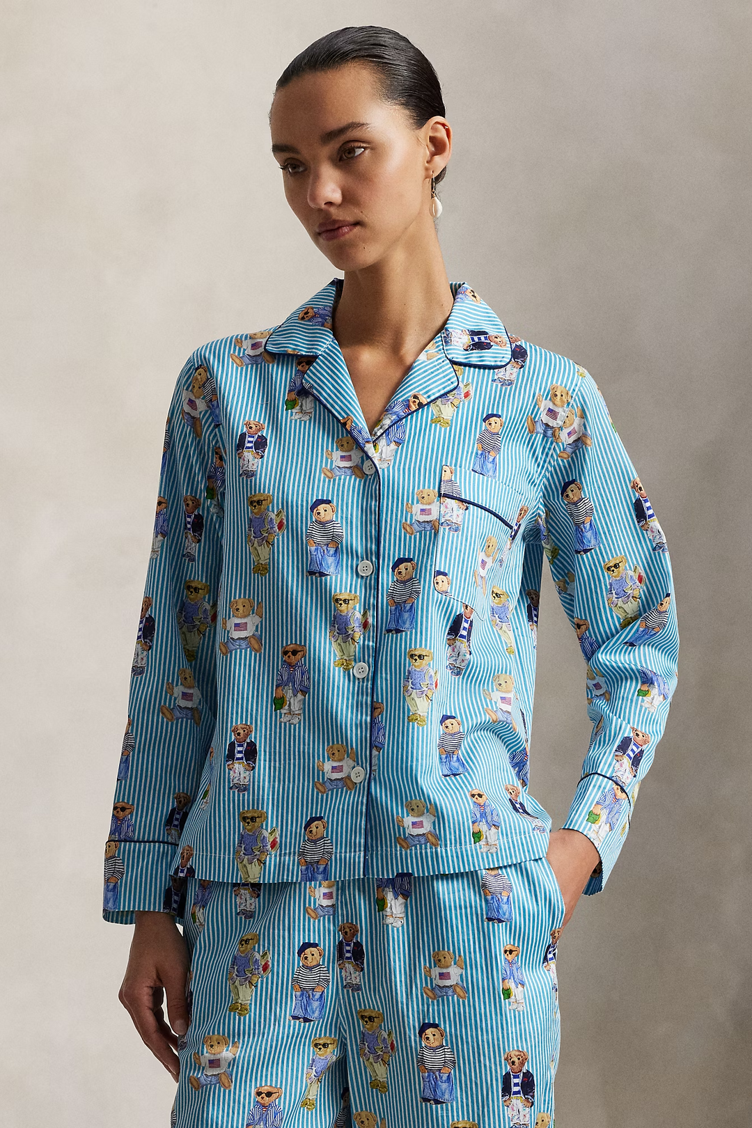 Woman wearing a polo ralph lauren blue striped pajama set with polo bear pattern on a neutral background