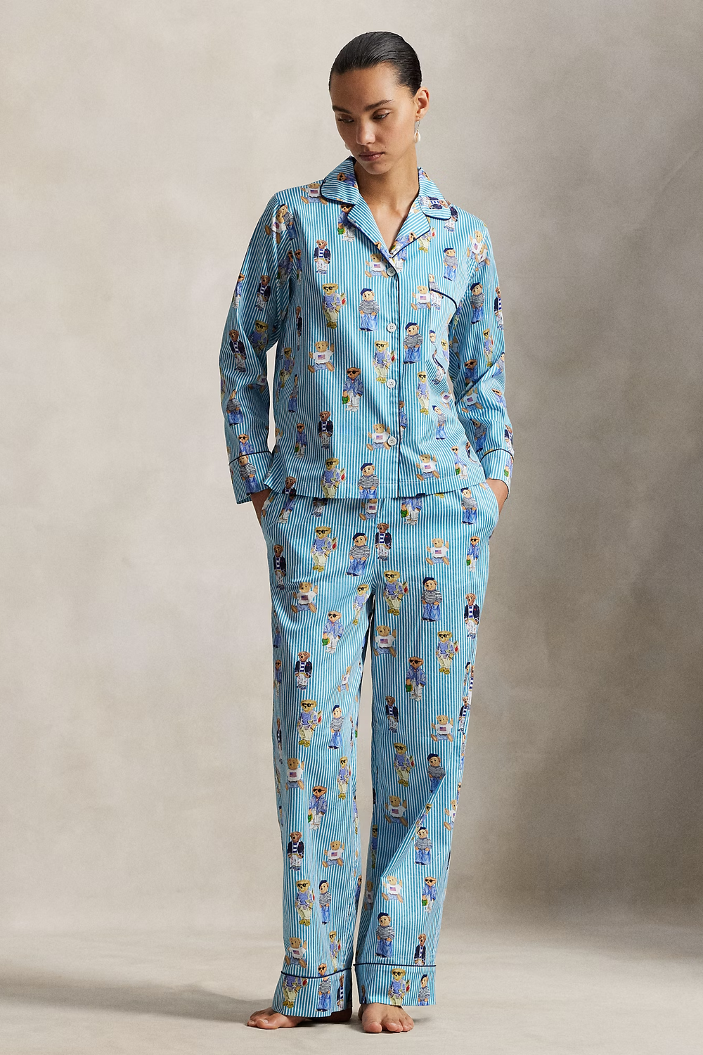 Woman wearing a polo ralph lauren blue striped pajama set with polo bear pattern on a neutral background