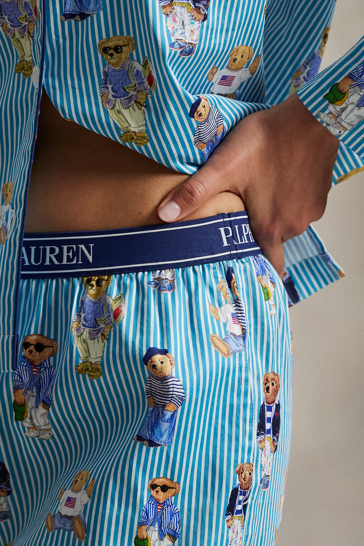 Woman wearing a polo ralph lauren blue striped pajama set with polo bear pattern on a neutral background