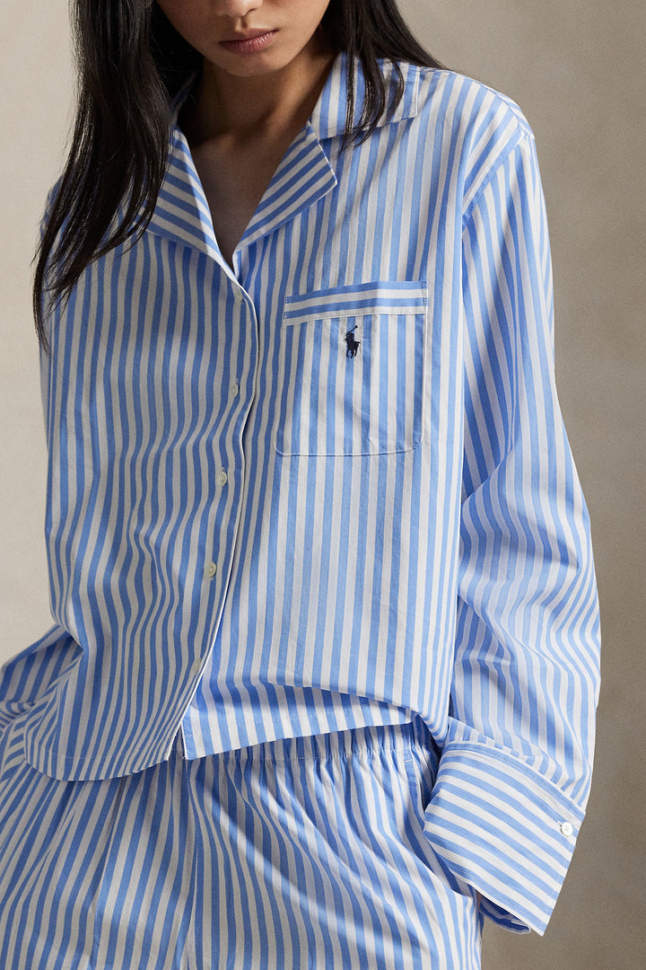 A close-up of a model wearing a blue and white vertically striped long-sleeve button-up shirt with a chest pocket featuring a small embroidered polo player logo, paired with matching striped bottoms.