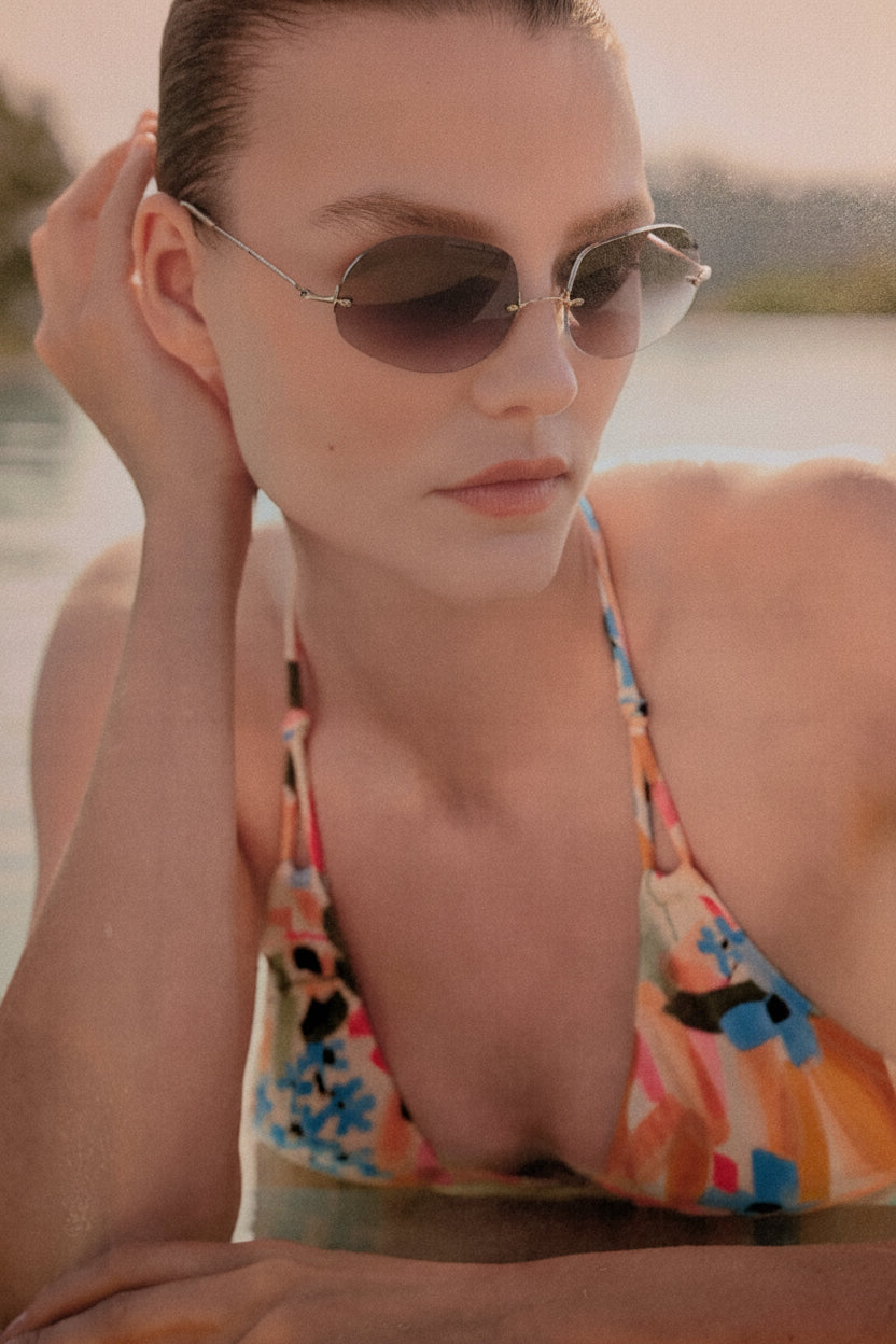 Woman wearing sunglasses and a colorful swimsuit by a body of water.