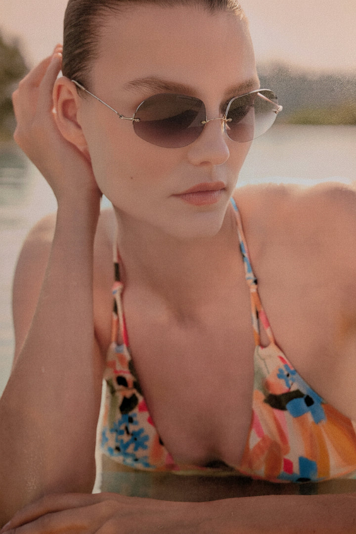 Woman wearing sunglasses and a colorful swimsuit by a body of water.