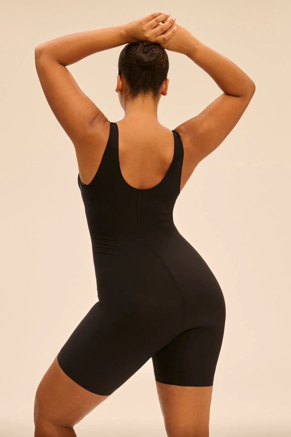 Person wearing a black bodysuit against a beige background