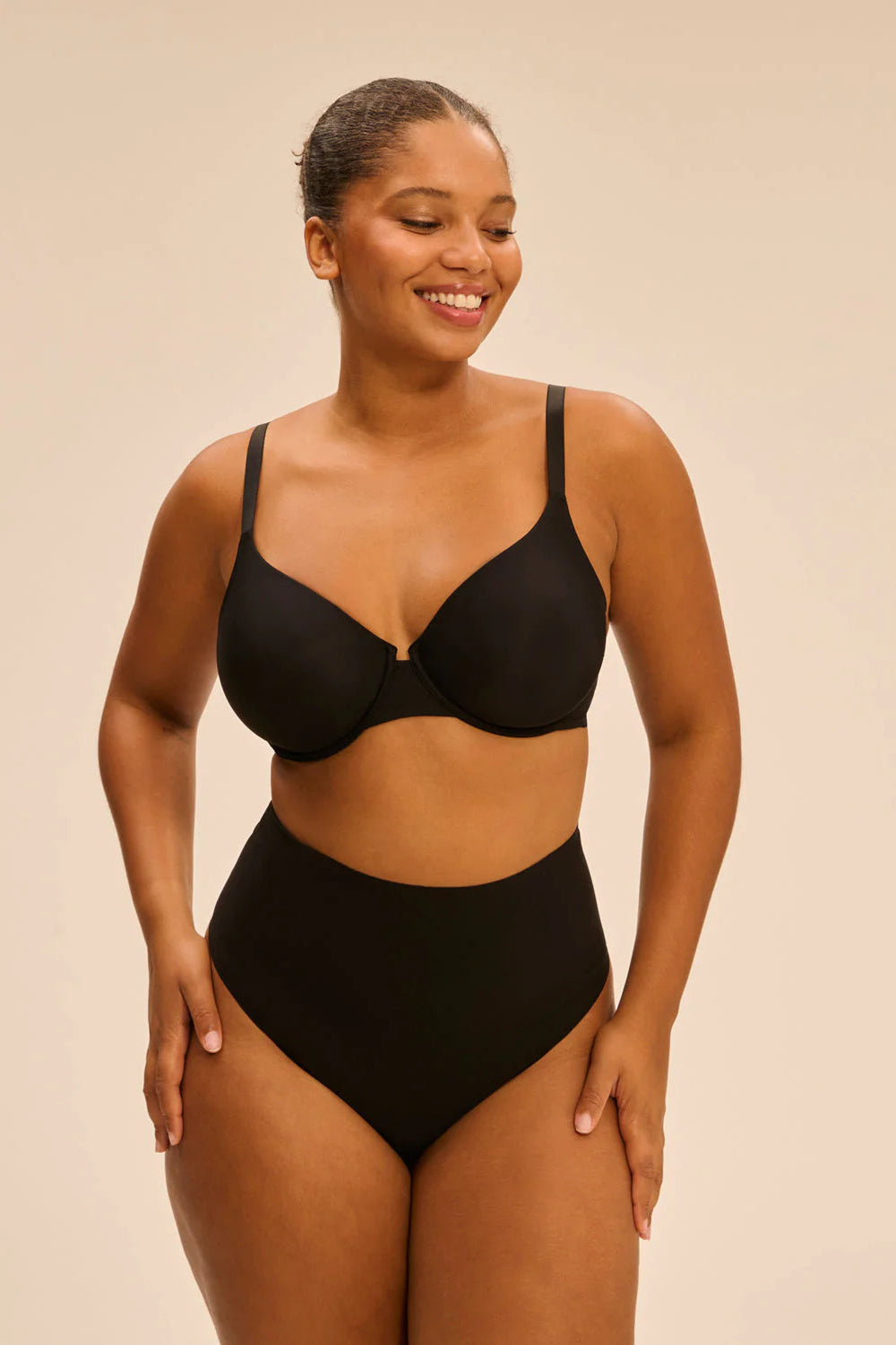 Woman wearing a black lingerie set on a beige background