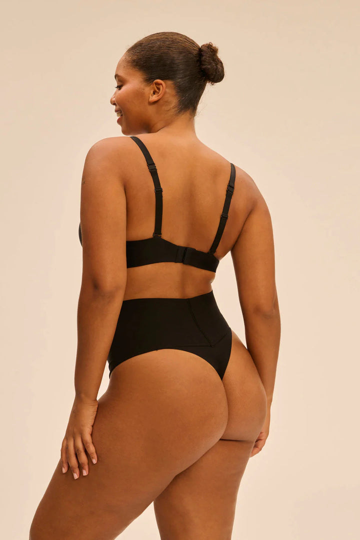 Woman wearing a black bikini set against a beige background