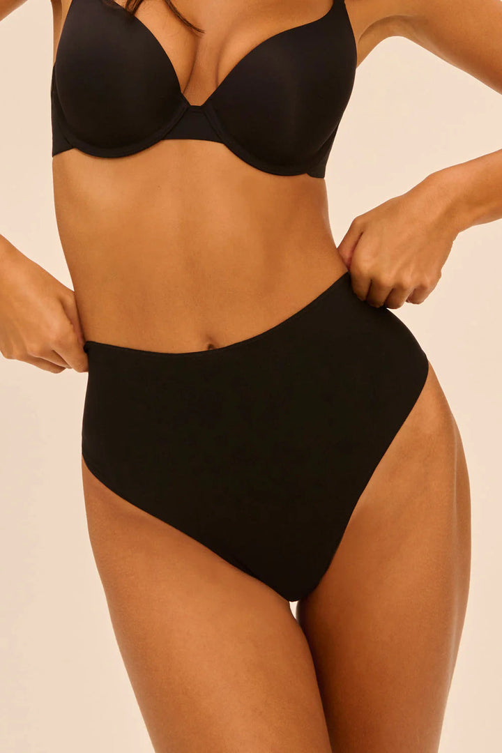 Person wearing a black shapewear panty against a beige background