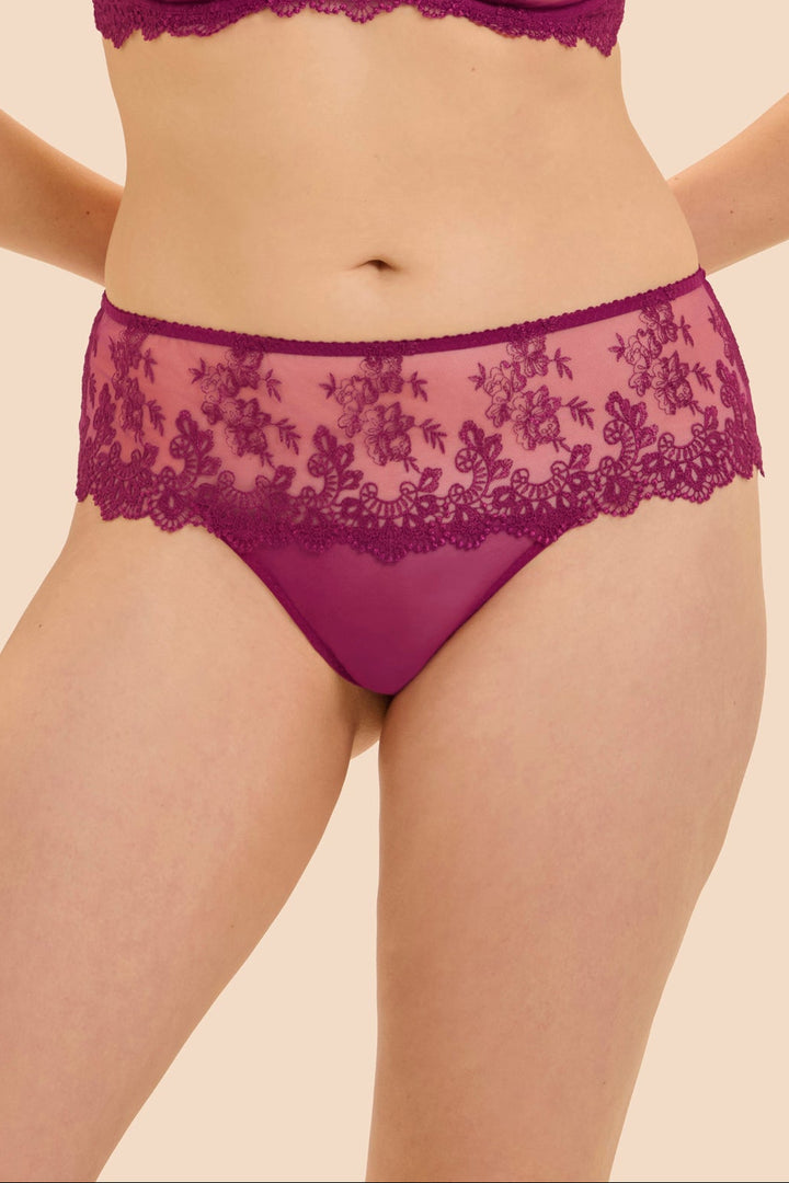 A model wearing a matching magenta lace bra and panty set against a solid beige background.