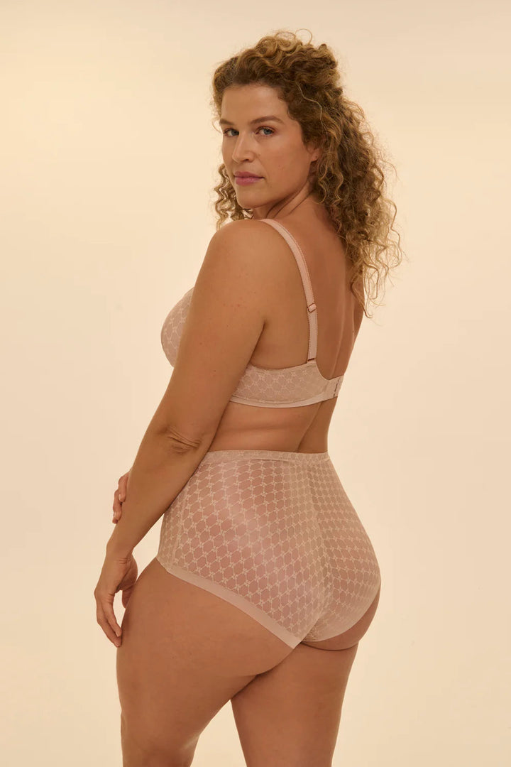 Woman wearing a beige seamless lace bra and panties set against a beige background