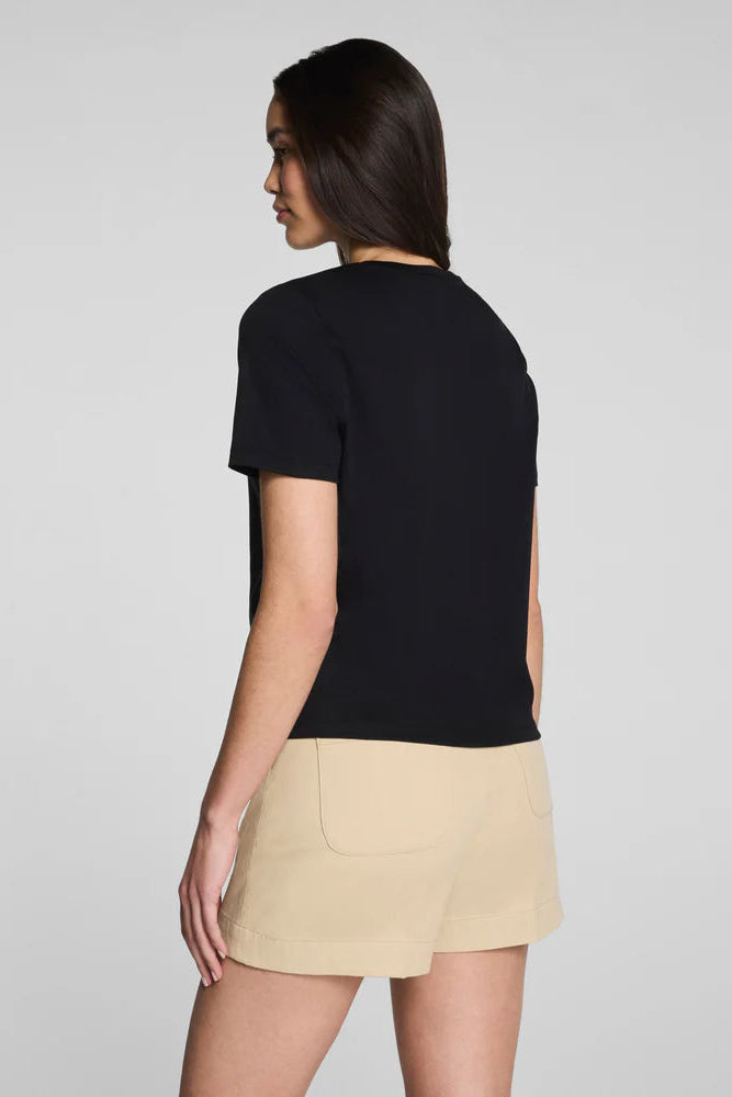 Woman wearing a black top and beige skirt on a plain background
