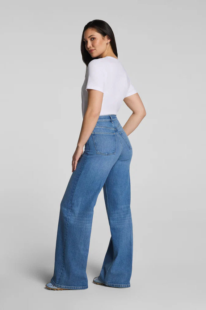 Woman wearing blue wide-leg jeans and a white t-shirt on a gray background